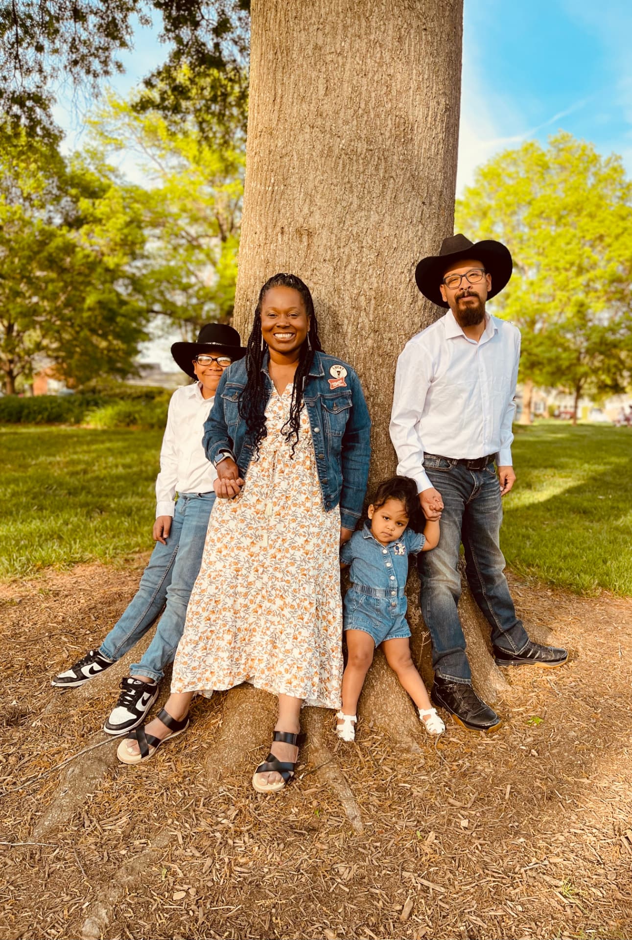Monique and Gregory Velasquez with their children Marcel and Mia, standing together by a large tree in a sunlit park